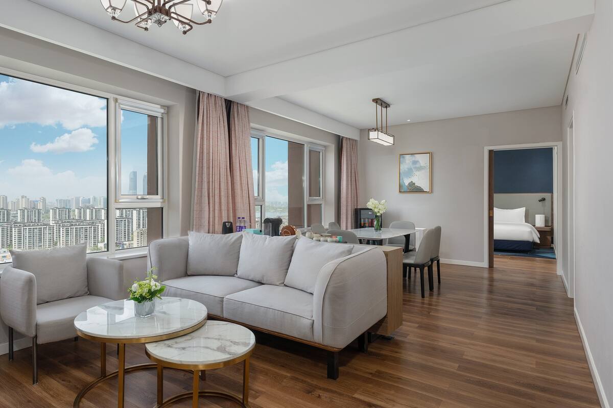 Una sala moderna con un sofá modular, una mesa de comedor y vistas de la ciudad a través de amplios ventanales.