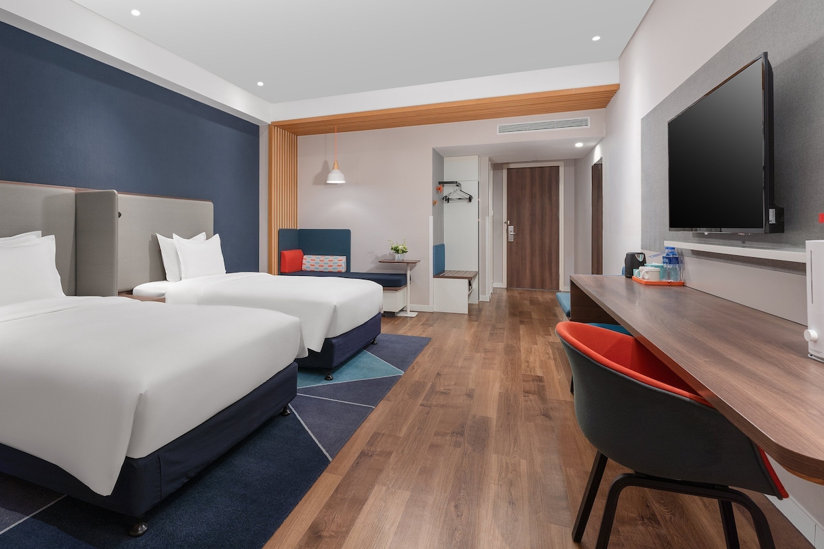 Une chambre d’hôtel avec deux lits, un bureau, une chaise, une télévision et une petite table avec une plante.
