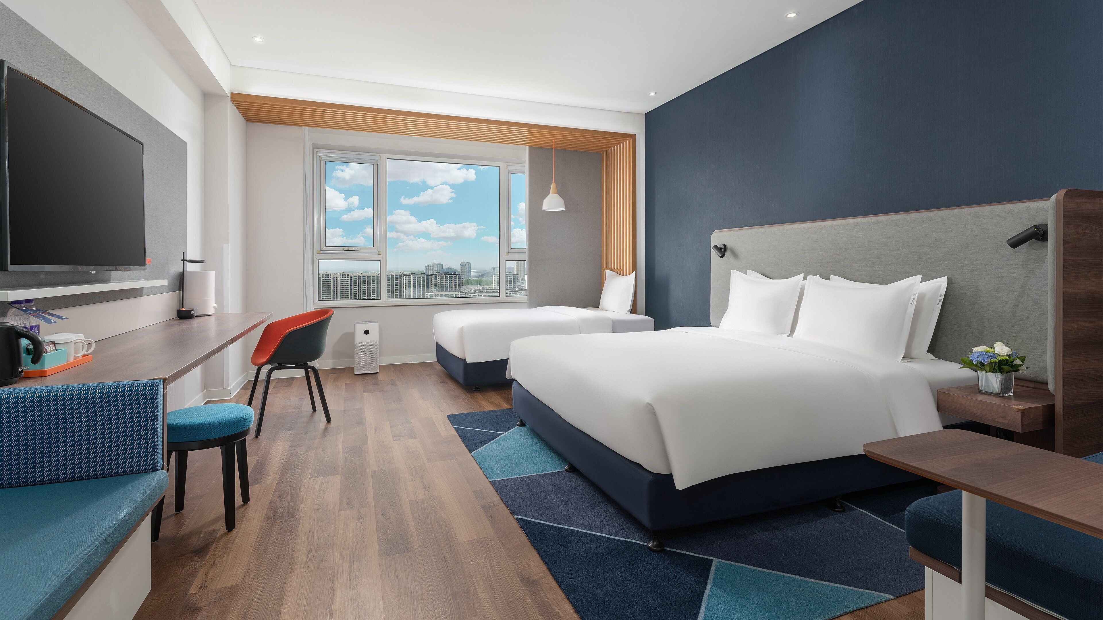 Habitación de hotel con una cama grande, un escritorio con silla, televisión y ventana con vista a la ciudad.