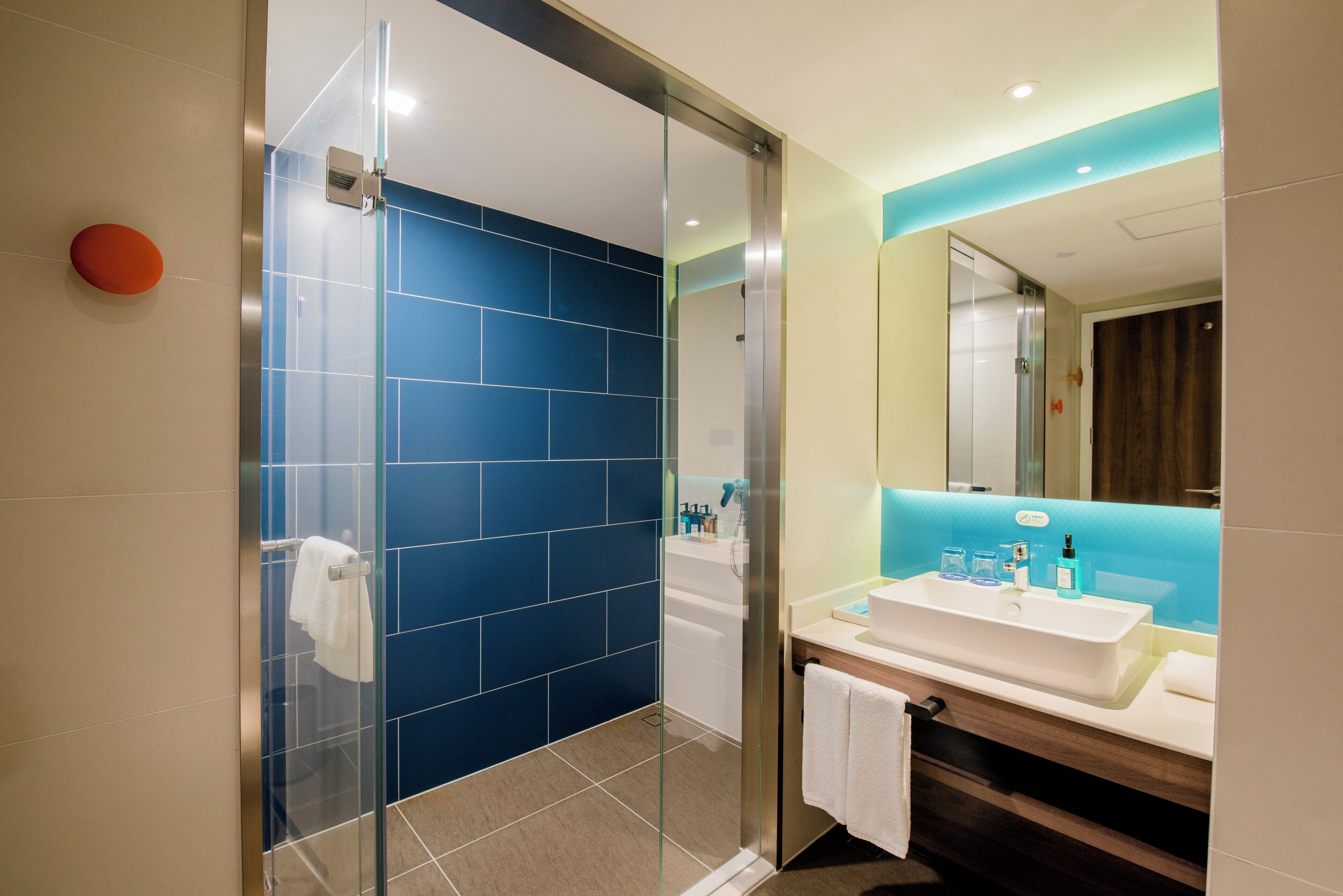 Un baño moderno con cabina de ducha de vidrio, un lavamanos blanco y un espejo encima.