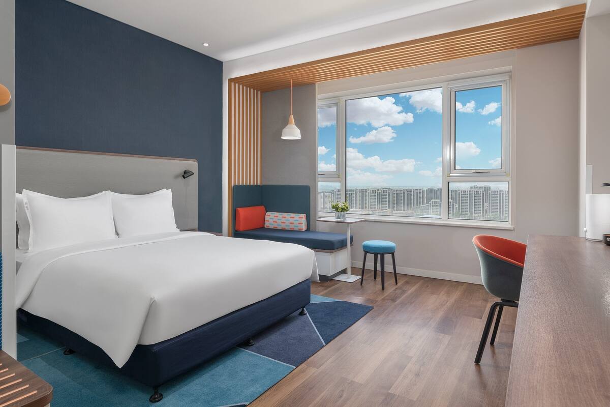 Una habitación de hotel moderna con una cama grande, una zona de estar con vistas y un televisor.