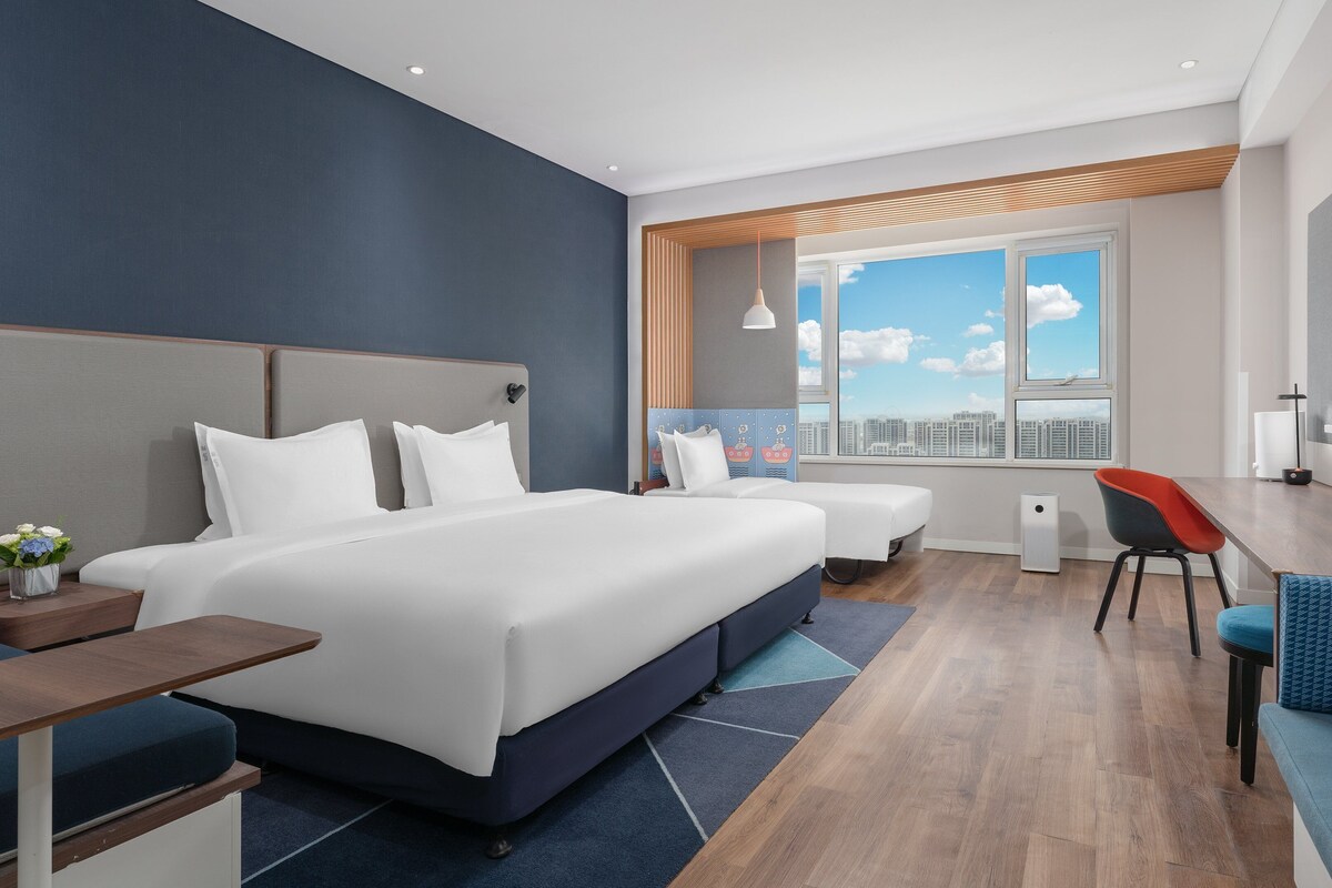 Une chambre d’hôtel moderne dotée d’un grand lit, d’un coin salon, d’une télévision et offrant une vue sur la ville.