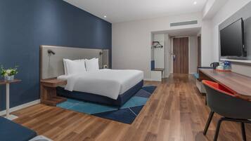 A modern hotel room with a large bed, a desk, and a seating area.