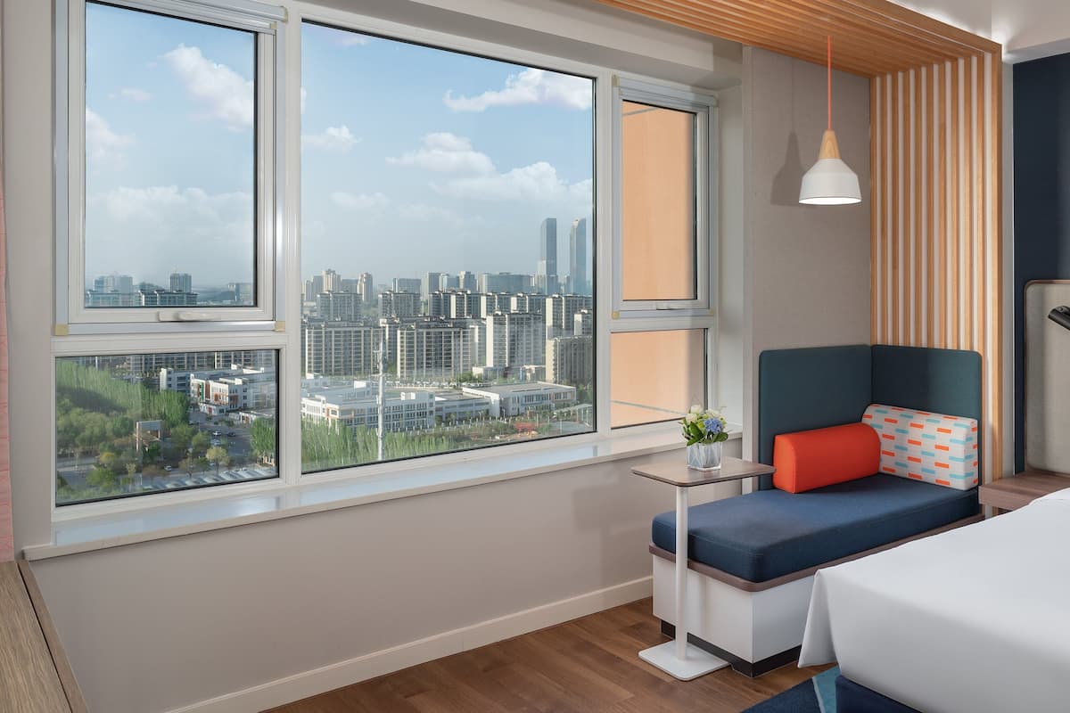Una habitación de hotel moderna con un ventanal grande, una cama, un área de descanso y vistas a la ciudad.
