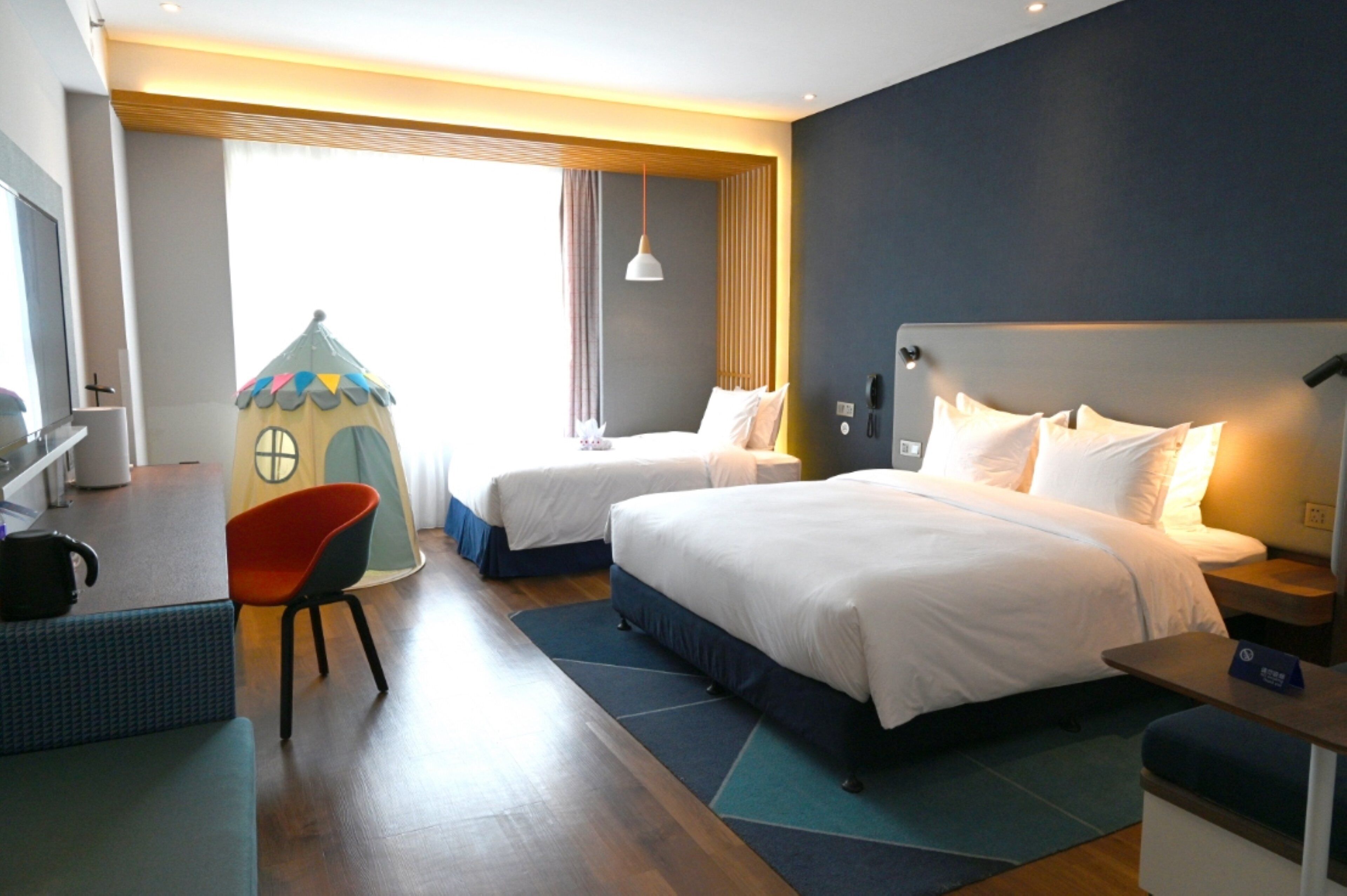 A hotel room with two beds, a play area, a desk, and a chair.