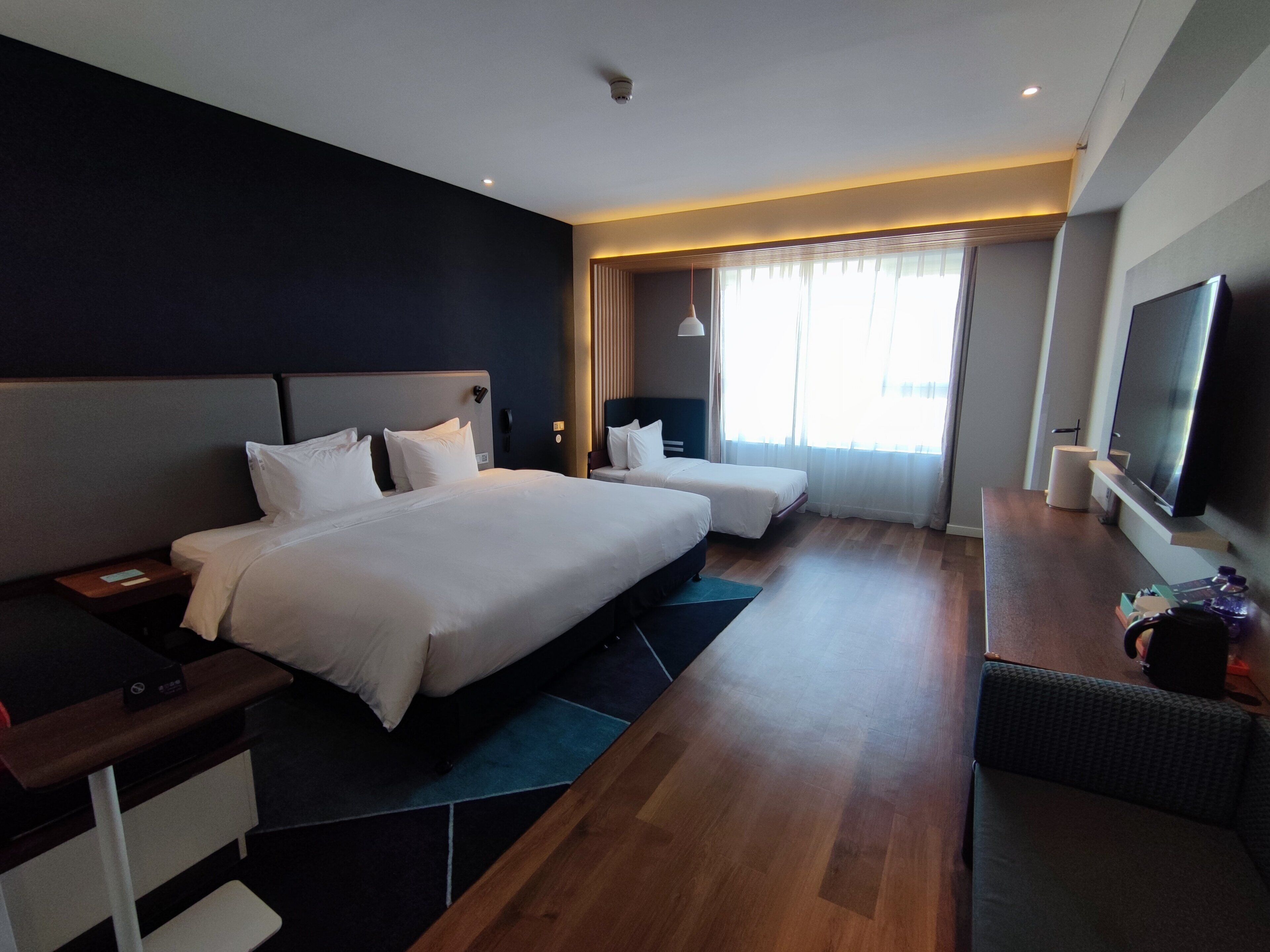 A modern hotel room with a large bed, a desk, a flat-screen TV, and a seating area.