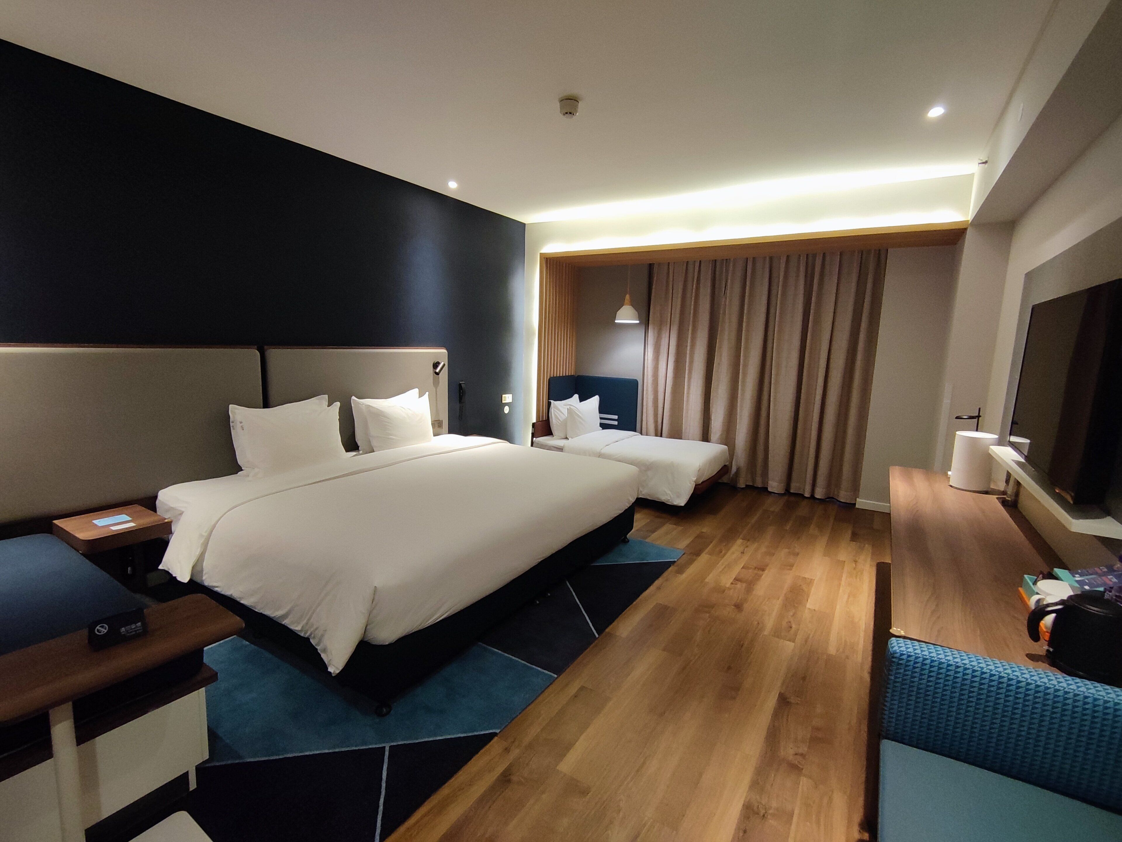 Quarto de hotel com uma cama grande, uma cama menor, uma mesa com telefone, televisão e banheiro.