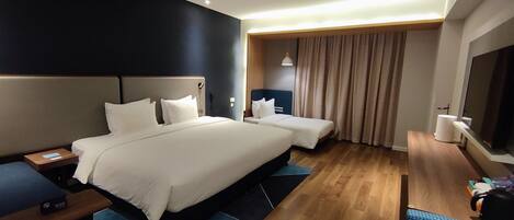 Quarto de hotel com uma cama grande, uma cama menor, uma mesa com telefone, televisão e banheiro.