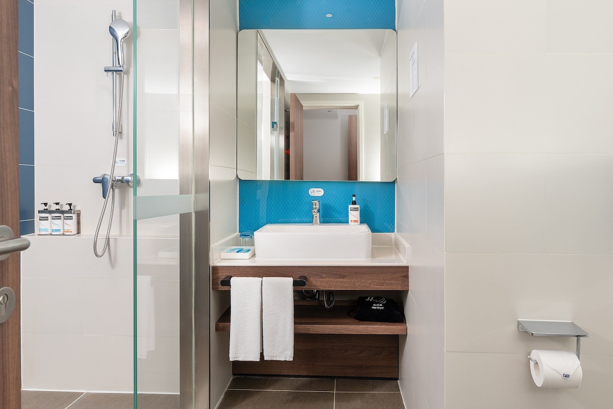Une salle de bain moderne avec une douche à l’italienne en verre, un lavabo blanc agrémenté d’un mur d’accent bleu et un meuble-lavabo en bois.