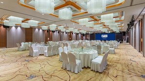 Une salle de banquet avec des tables rondes, des chaises blanches et des lustres.