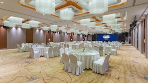 Une salle de banquet avec des tables rondes, des chaises blanches et des lustres.