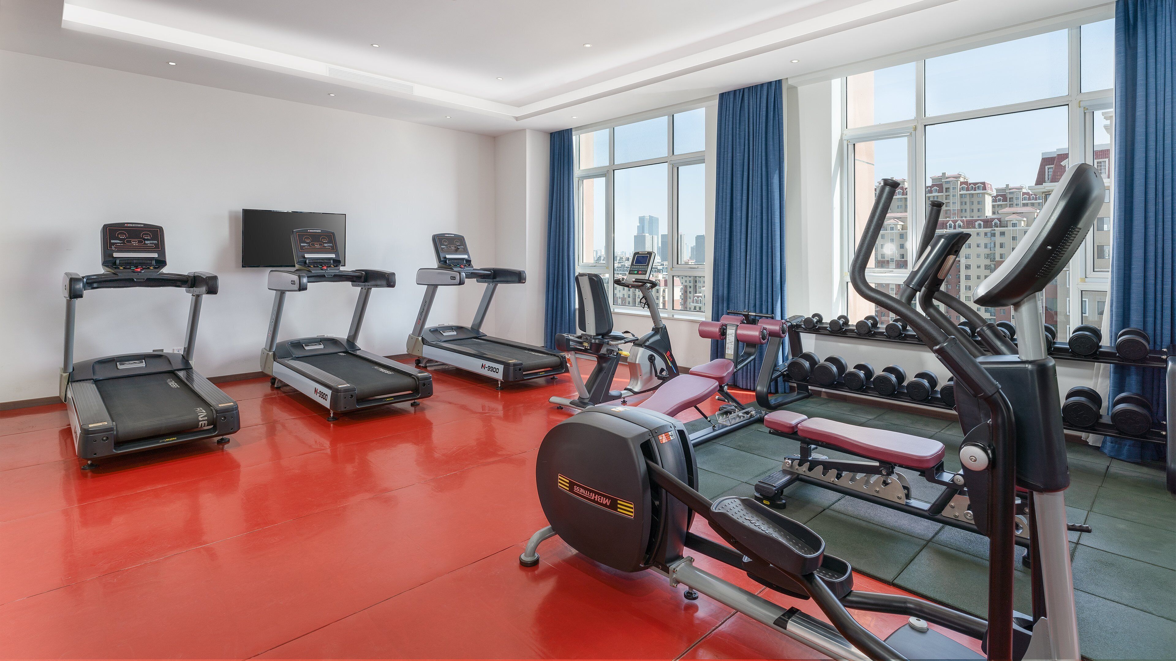 Une salle de sport équipée de tapis de course, d’un appareil elliptique et d’un banc de développé couché.