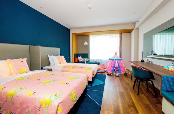 Une chambre d’hôtel avec deux lits, un bureau, une chaise, une fenêtre avec des rideaux et une petite tente de jeu.
