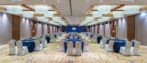 A conference room with rows of tables and chairs, a patterned carpet, and modern chandeliers.