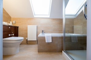 A modern bathroom with a skylight, a freestanding bathtub, a toilet, and a glass shower enclosure.