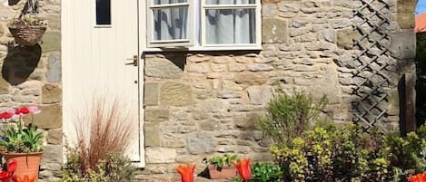 Una casa de piedra con tejado de baldosas, una puerta blanca con el número 9 y una ventana con cortinas.