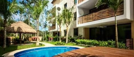A modern hotel with a swimming pool, wooden deck, and lush greenery.