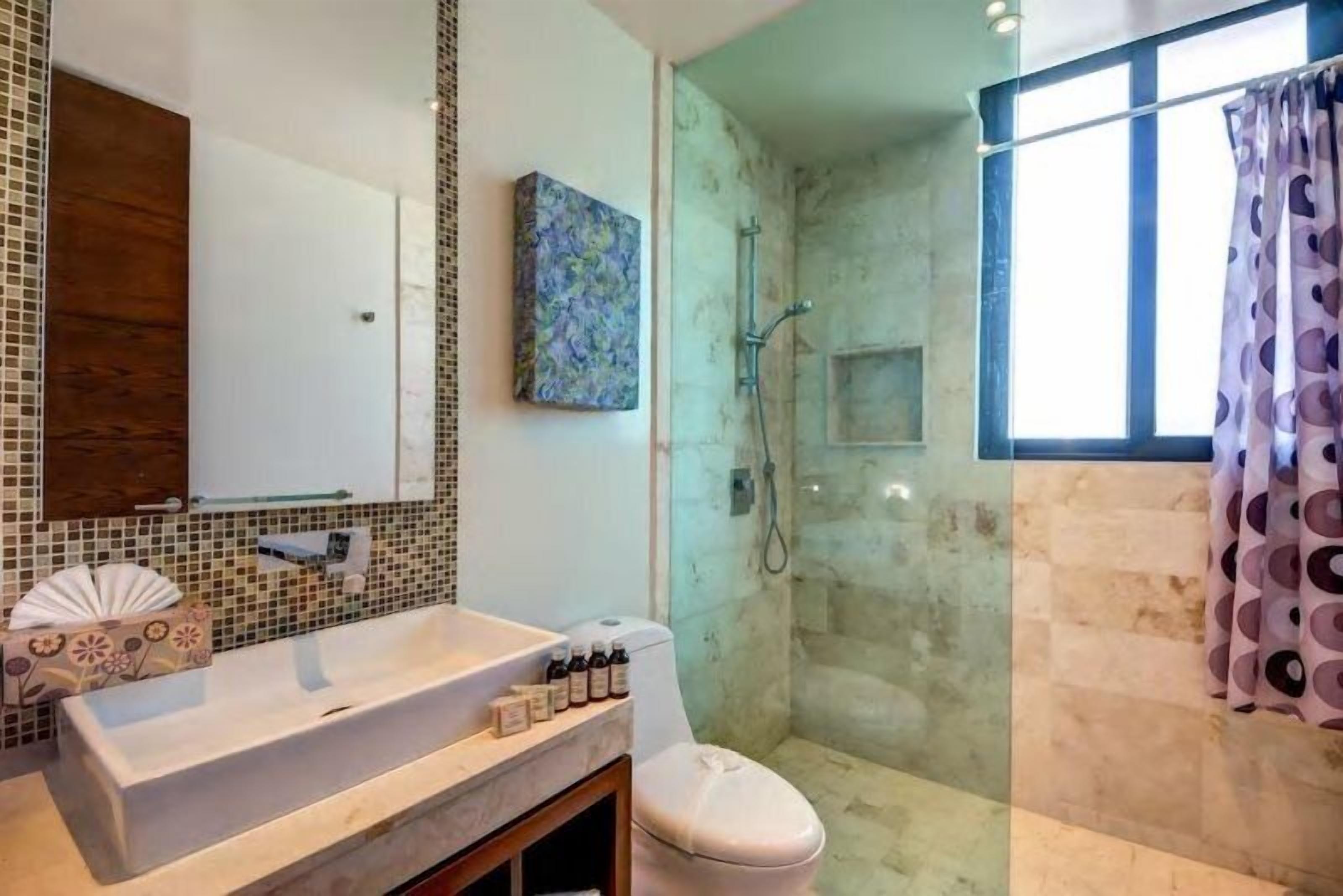 A bathroom with a large mirror, a sink, a toilet, and a shower area.