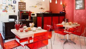 A dining area with red chairs and tables, a kitchen in the background, and various kitchen appliances. - Sosta dei Garibaldini (Campofelice di Roccella)