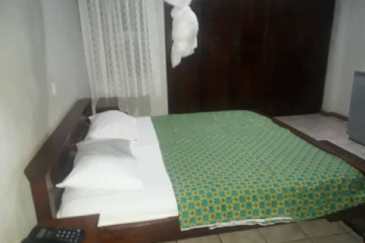 A bed with a patterned bedspread, a bedside table with a remote control, and a curtain.