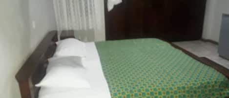 A bed with a patterned bedspread, a bedside table with a remote control, and a curtain.