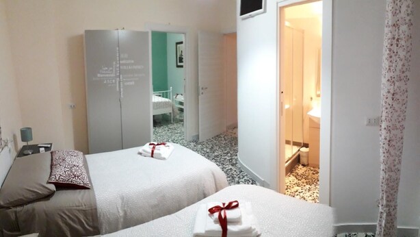 A hotel room with two beds, a wardrobe, and a bathroom visible through an open door. - Edelweiss B&B (Salerno)