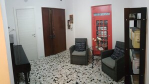 A room with a white door, a red telephone booth, two armchairs, a small table, and a bookshelf. - Edelweiss B&B (Salerno)