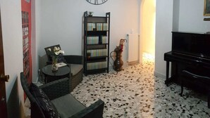 A living room with a black piano, a bookshelf, a clock, and a red door. - Edelweiss B&B (Salerno)