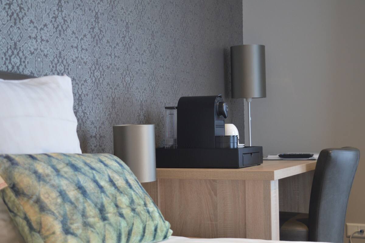 Een hotelkamer met een bed, een bureau met koffiezetapparaat, een lamp en een stoel.