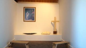 Une petite chapelle avec des bancs en bois, un crucifix en bois et un tableau encadré accroché au mur.