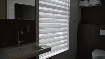 Un baño con lavamanos, inodoro y ventana con persianas.