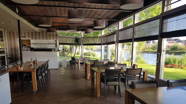 Een modern restaurant met houten vloeren, grote ramen en uitzicht op een meer.