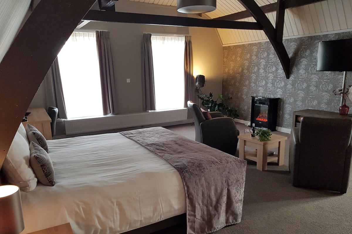 Een slaapkamer met een bed, een bureau, een stoel, een open haard en een raam met gordijnen.