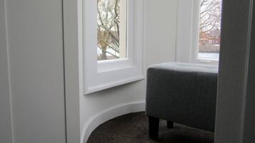 A corner room with a window, a grey upholstered bench, and a carpeted floor.
