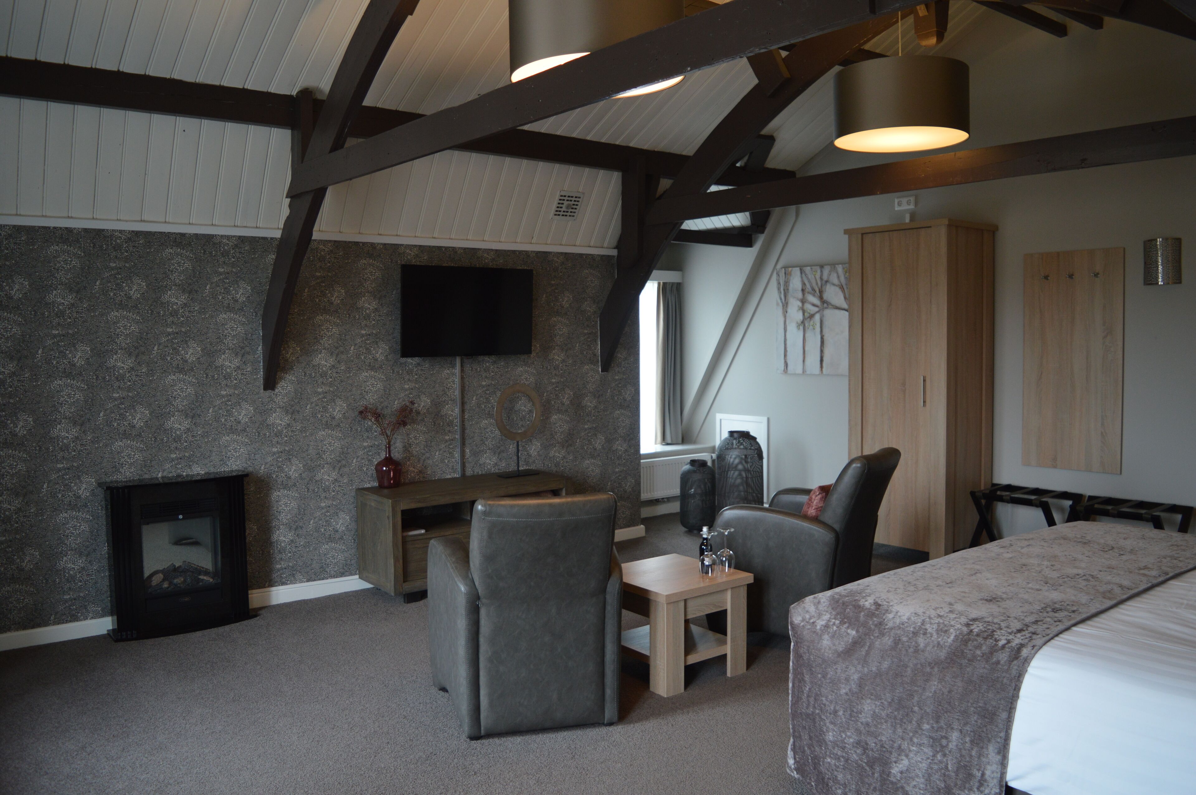A modern bedroom with a sloped ceiling, a fireplace, a desk, and a bed.
