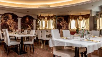 Un restaurant avec des tables rondes, des nappes blanches et une fresque florale sur les murs.
