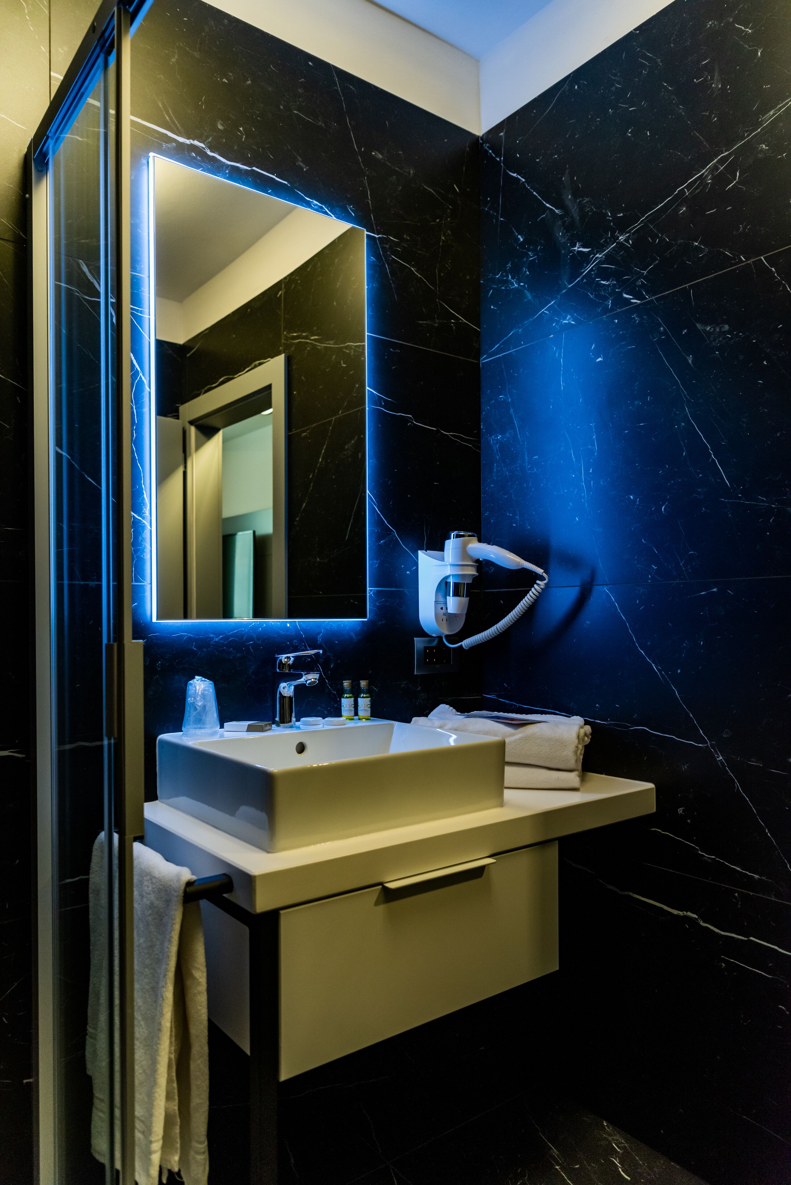 A modern bathroom with a large mirror, a built-in hairdryer, and a vanity with a sink and towel rack.