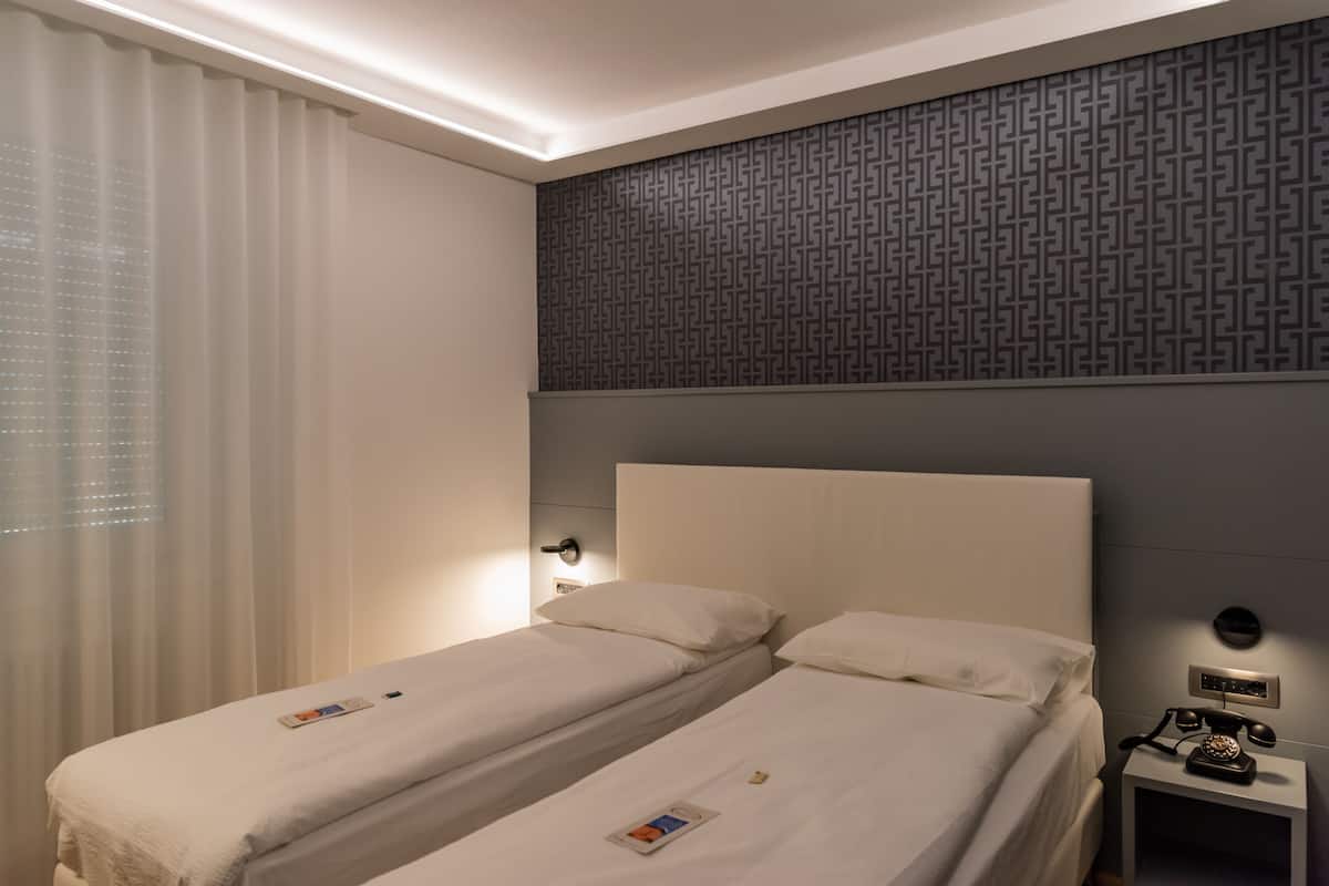 Une chambre d’hôtel avec deux lits simples, une table de chevet avec un téléphone et un mur orné d’un motif géométrique.