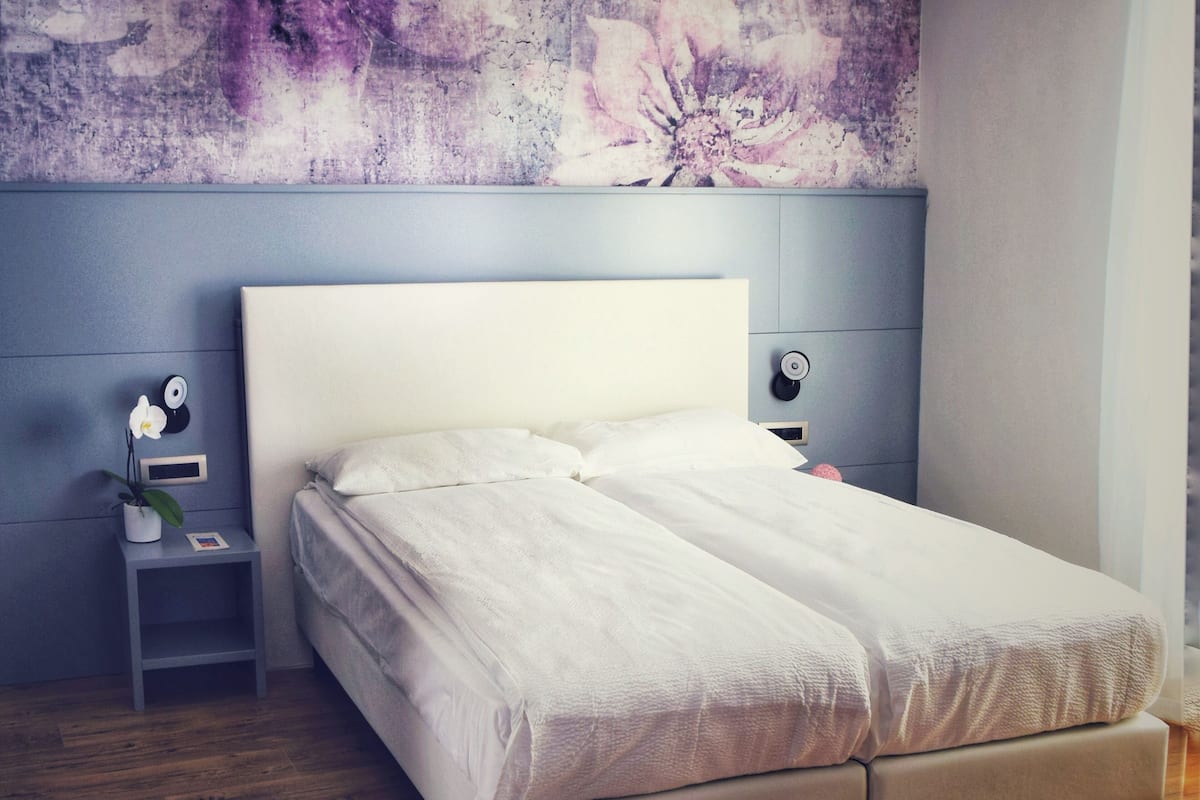 Une chambre à coucher comprenant un lit, une table de chevet, une lampe fixée au mur et une décoration murale à motifs floraux.