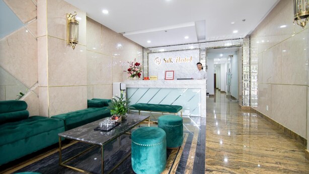 A hotel reception area with a marble reception desk, green upholstered seating, and a marble floor. - Silk Hotel (Ho Chi Minh City)