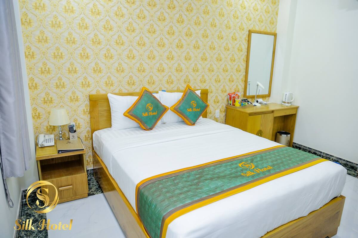 A hotel room with a bed, a nightstand, a bedside table, a mirror, and a bathroom area.
