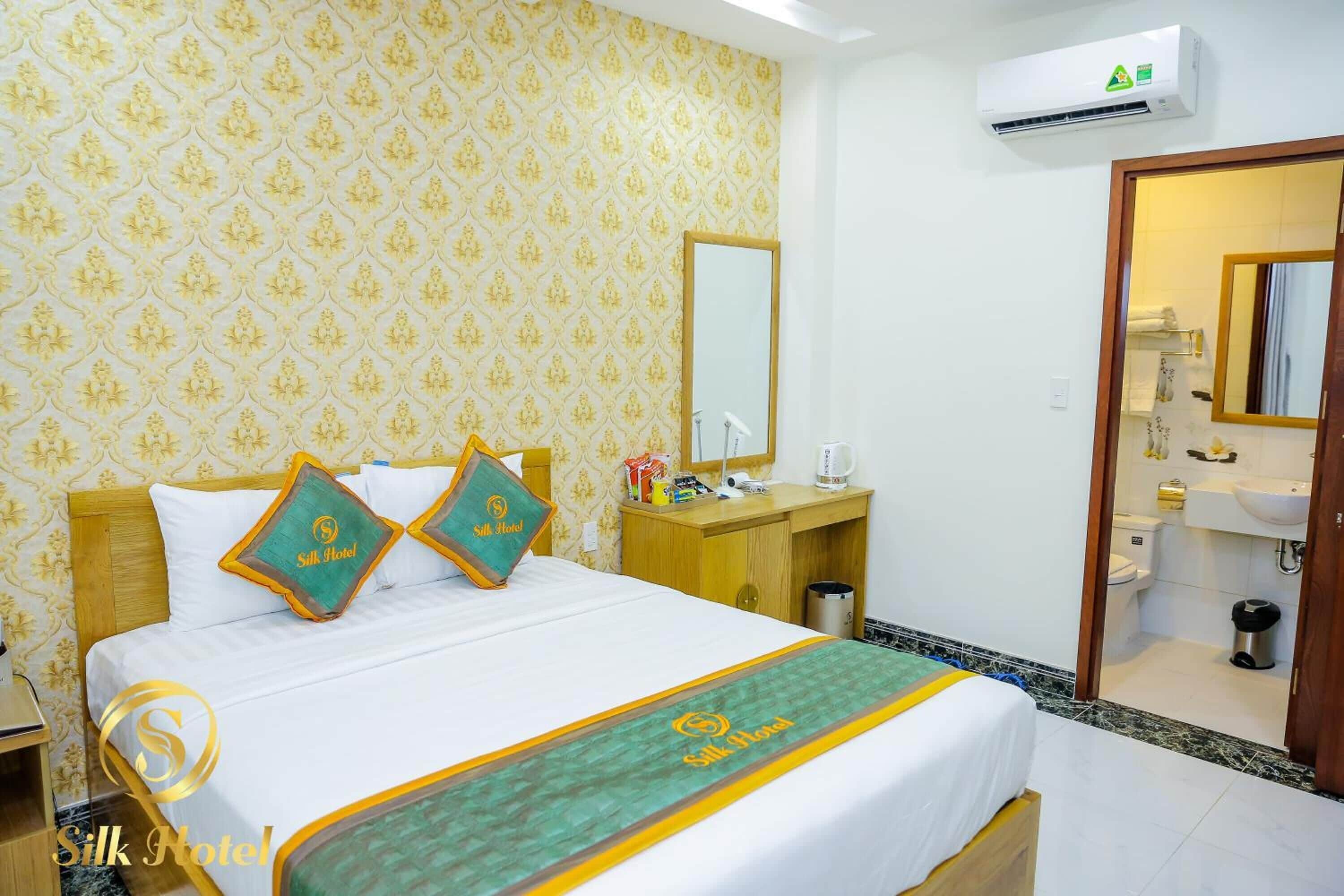 A hotel room with a bed, a nightstand, a mirror, and a bathroom visible through an open door.