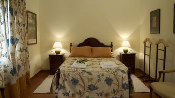Une chambre à coucher avec une couvre-lit à motifs floraux, deux lampes de chevet, une tête de lit en bois et une chaise.
