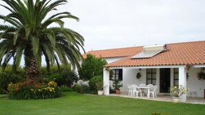 Un edificio blanco con techo de tejas y un patio cubierto con sillas blancas.