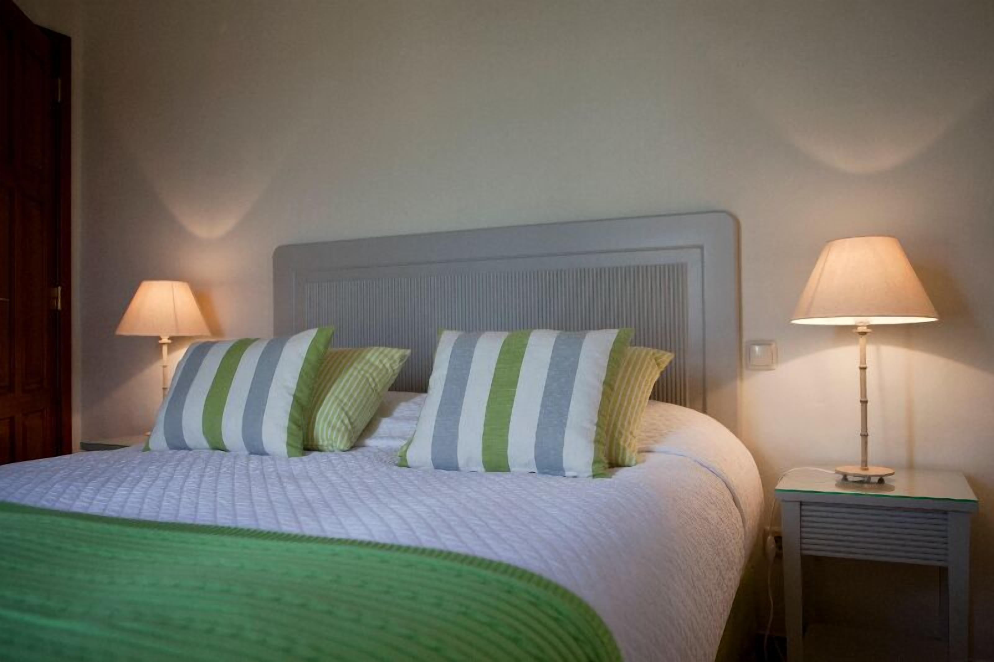 A neatly made bed with striped pillows, a green throw blanket, and two bedside lamps on white nightstands.