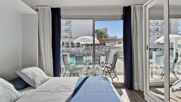 Ein Hotelzimmer mit Balkon, einem Bett und einer Sitzecke mit Stühlen und Sonnenschirmen.
