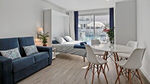 Ein modernes Hotelzimmer mit einem Bett, einem blauen Sofa, einem Esstisch mit Stühlen und einer Topfpflanze.