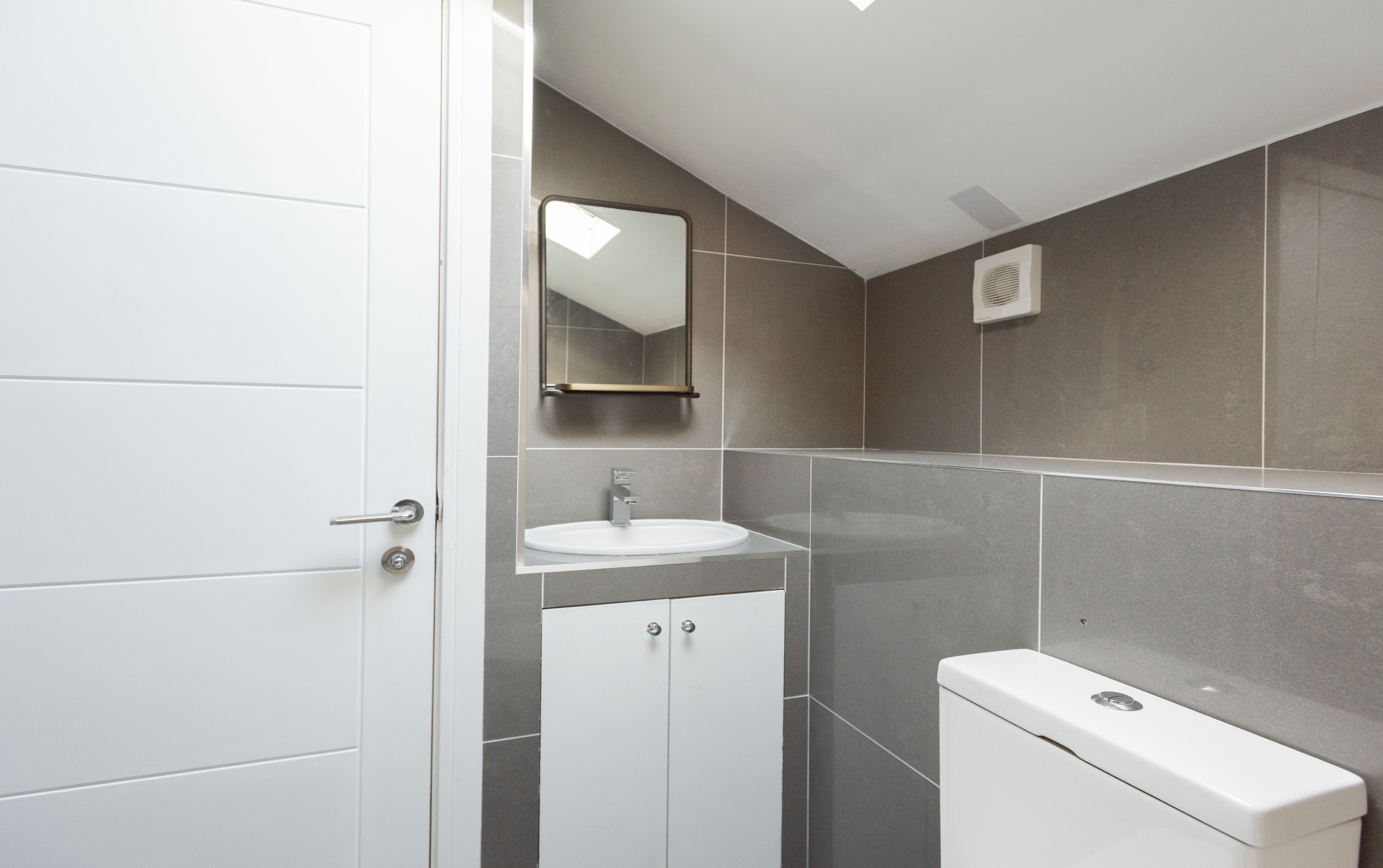 A modern bathroom with a white door, a sink, a mirror, and a toilet.