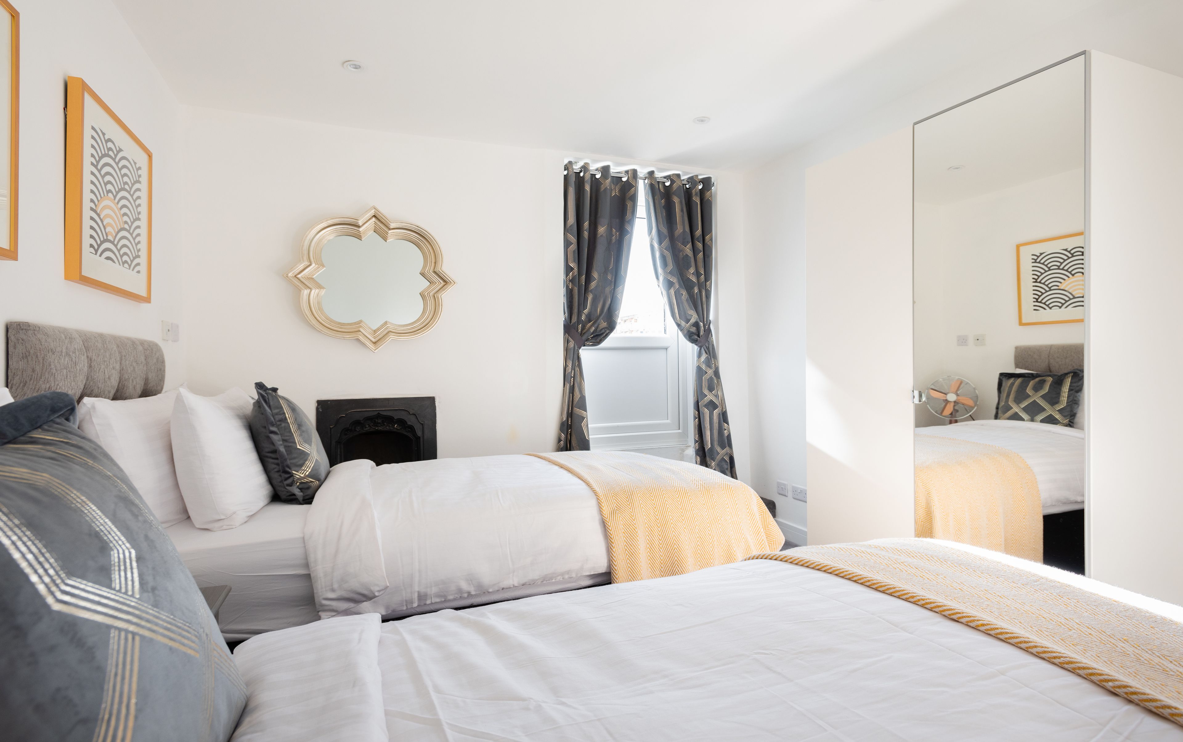 A modern bedroom with a large bed, a bedside table, a mirror, and a window with curtains.