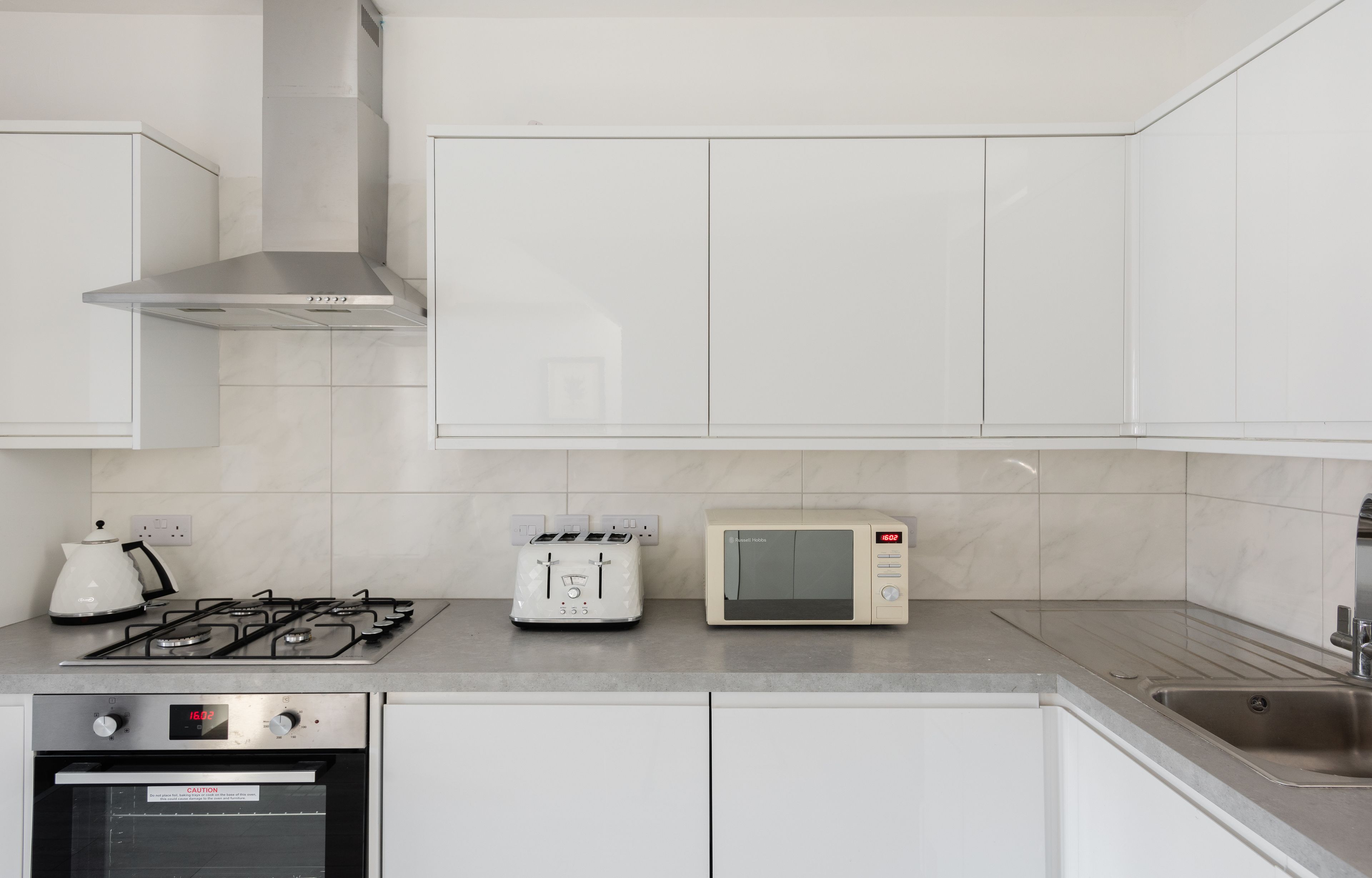 Une cuisine moderne avec des meubles blancs, une cuisinière à gaz, un grille-pain et un four à micro-ondes.